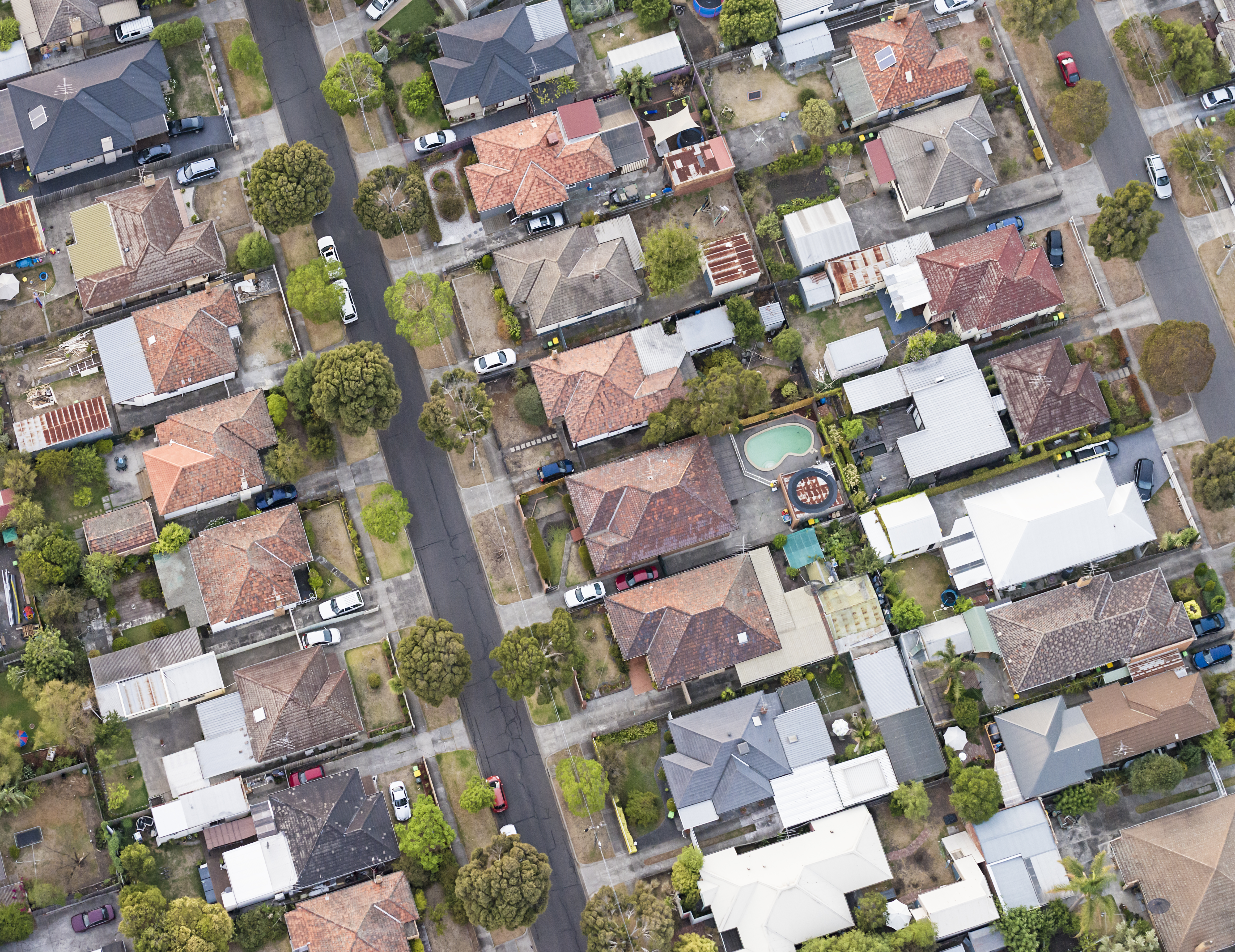 A view of suburban detached houses, gardens, streets and cars from directly above.